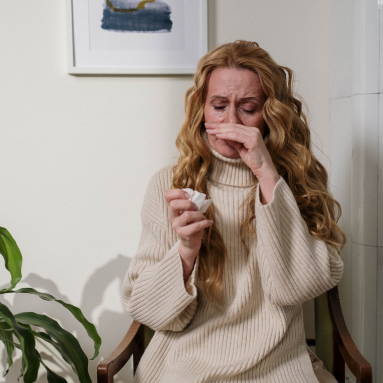Femme présentant des symptômes d'allergie au pollen avec les yeux larmoyants, le nez irrité et un mouchoir à la main.