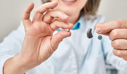 Praticien tenant un appareil auditif dans une main et une pile dans l’autre Praticien tenant un appareil auditif dans une main et une pile dans l'autre, illustrant les accessoires pris en charge par la mutuelle et la Sécu