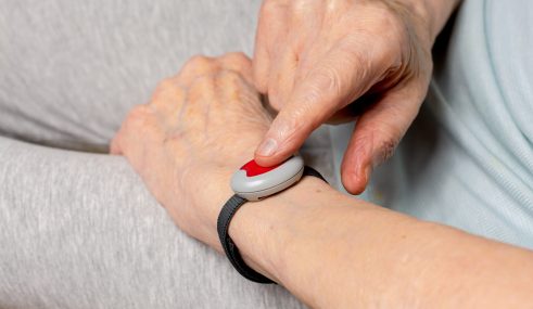 Bracelet de téléassistance pour retraités et séniors Femme âgée portant une montre de téléassistance et appuyant sur le bouton d’alerte pour demander de l’aide.